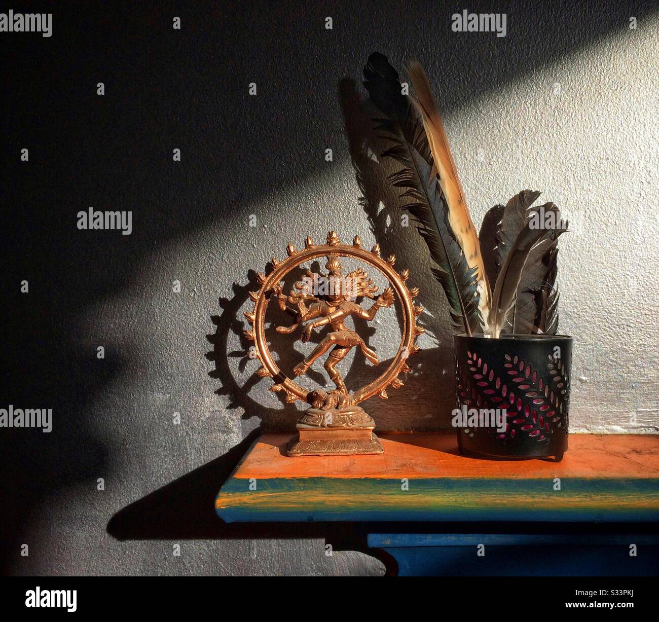 A colourful shelf holding a bronze dancing Shiva statuette and some birds feathers, shadow and light, new age spiritual with copy space - Smartphone Captured Stock Image
