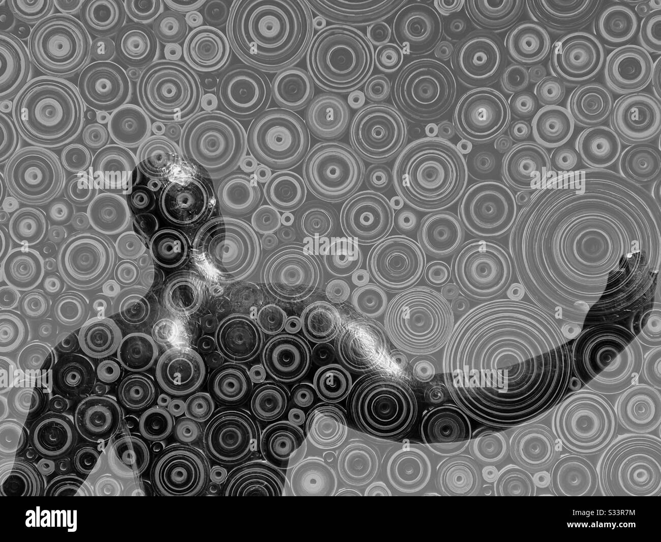 Overlapping art works - the back of a sculpture of a muscular woman and an abstract painting of circles - in black and white Stock Photo