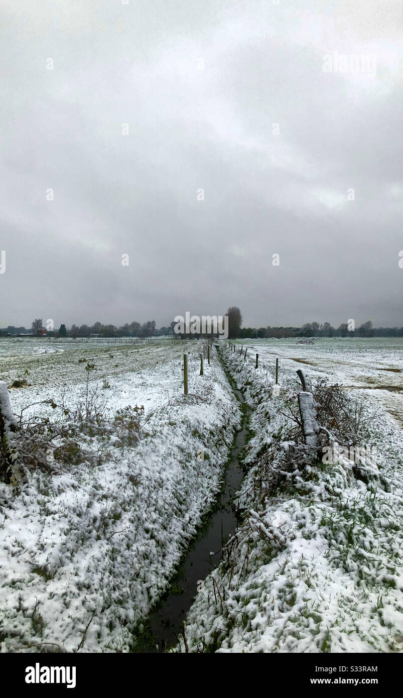 Two farmfields divided by a creek and under a blanket of snow with a grey cloudy snow filled sky above - Smartphone Captured Stock Image