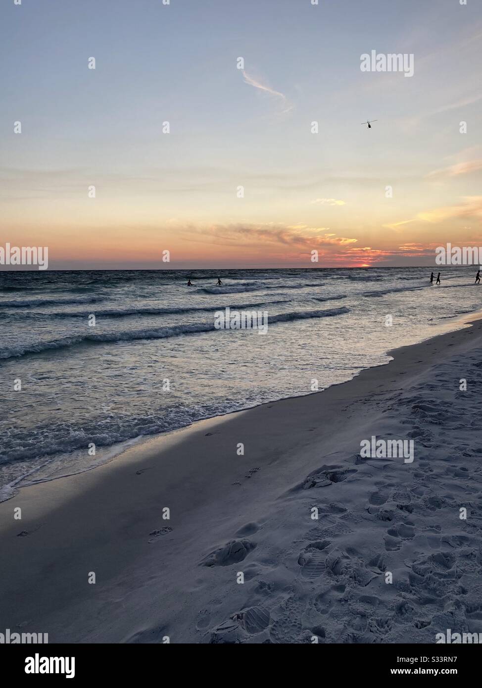 Golden sunset skies with silhouettes of people in the water on the beach - Smartphone Captured Stock Image