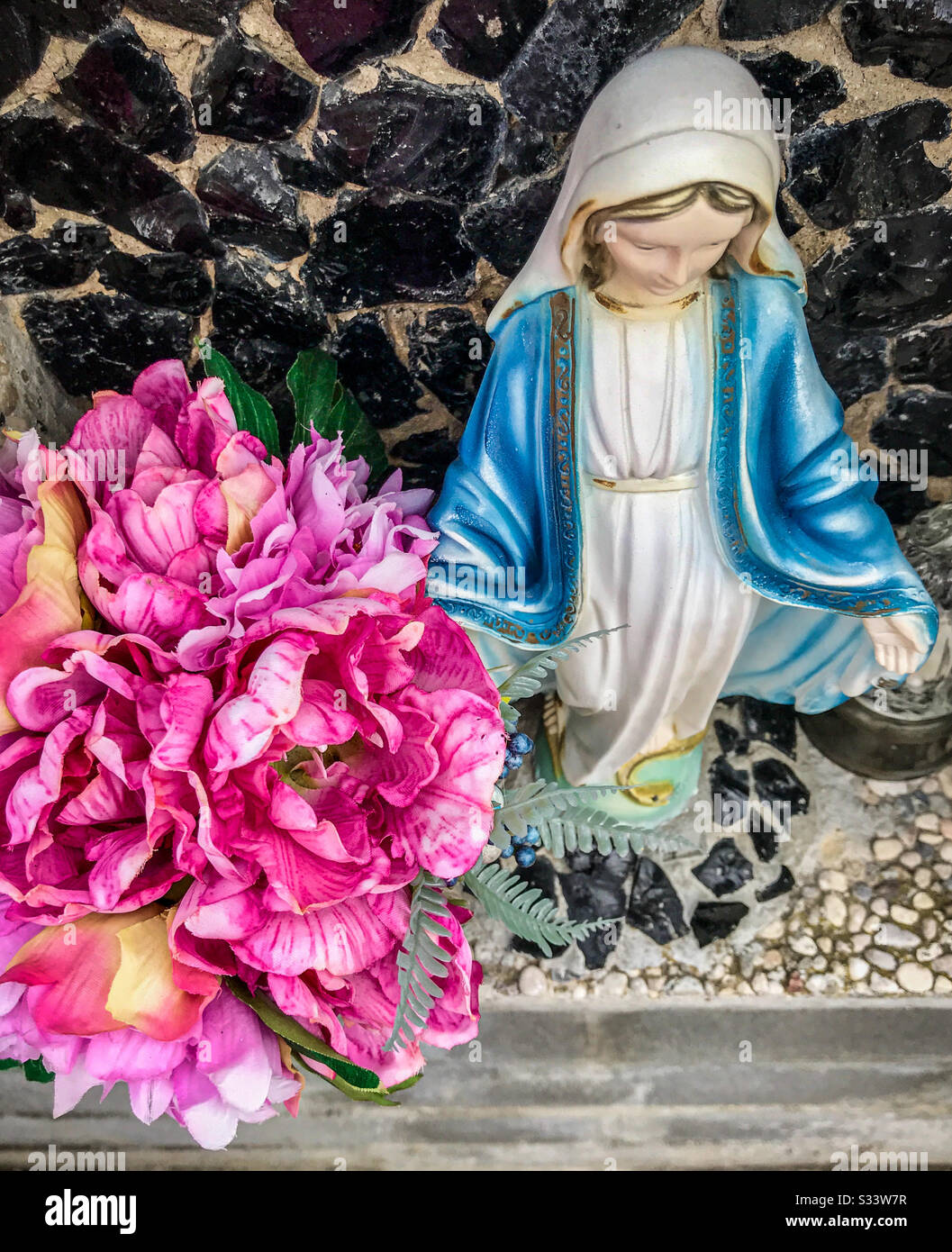 A photo of a Virgin Mary statue and pink silk flowers Stock Photo ...
