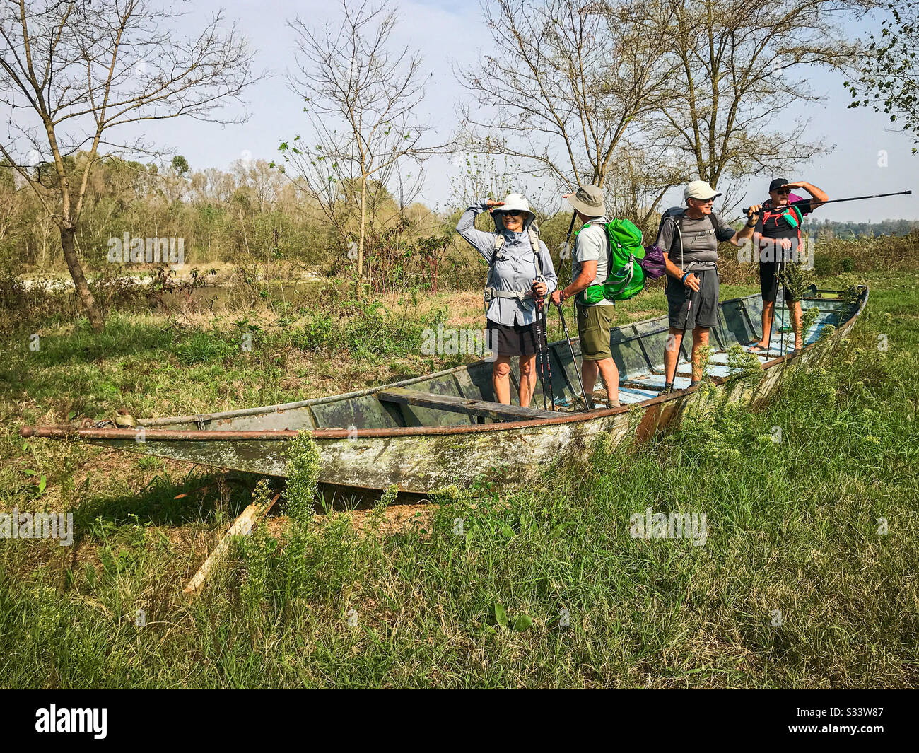 Four adult backpackers having fun while standing in a row boat that is sitting in a grass field. No water. - Smartphone Captured Stock Image