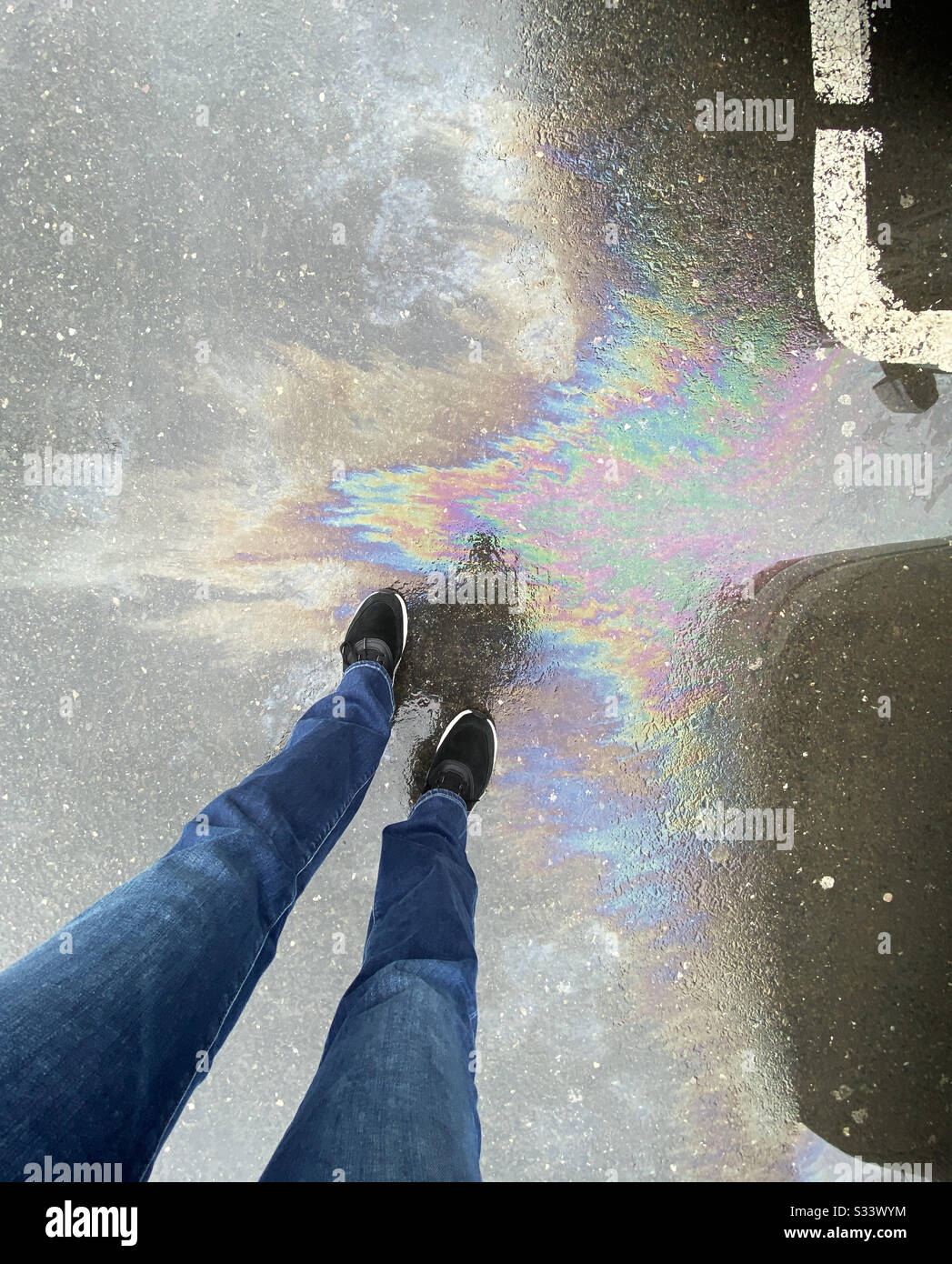 View of woman’s legs and oil spill on asphalt - Smartphone Captured Stock Image