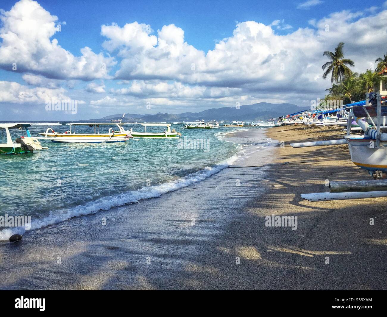 Traditional Balinese outrigger fishing boats, also used to ferry tourists on sightseeing, diving or snorkelling trips, Candidasa Beach, Bali, Indonesia - Smartphone Captured Stock Image