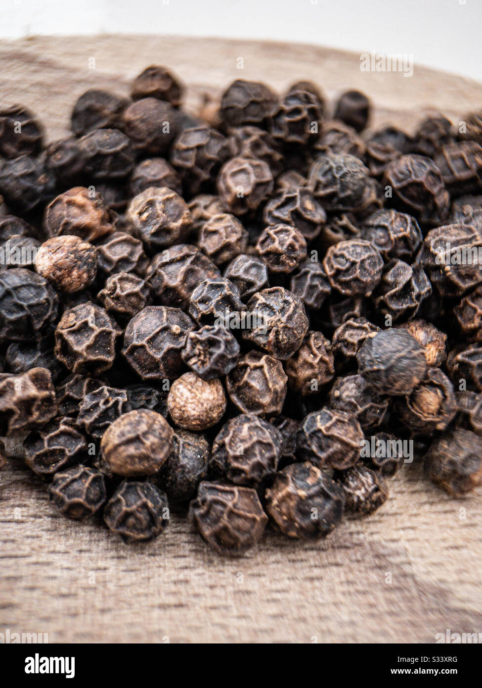 Black peppercorns on a wooden board.  Close up of raw pepper.  Macro - Smartphone Captured Stock Image
