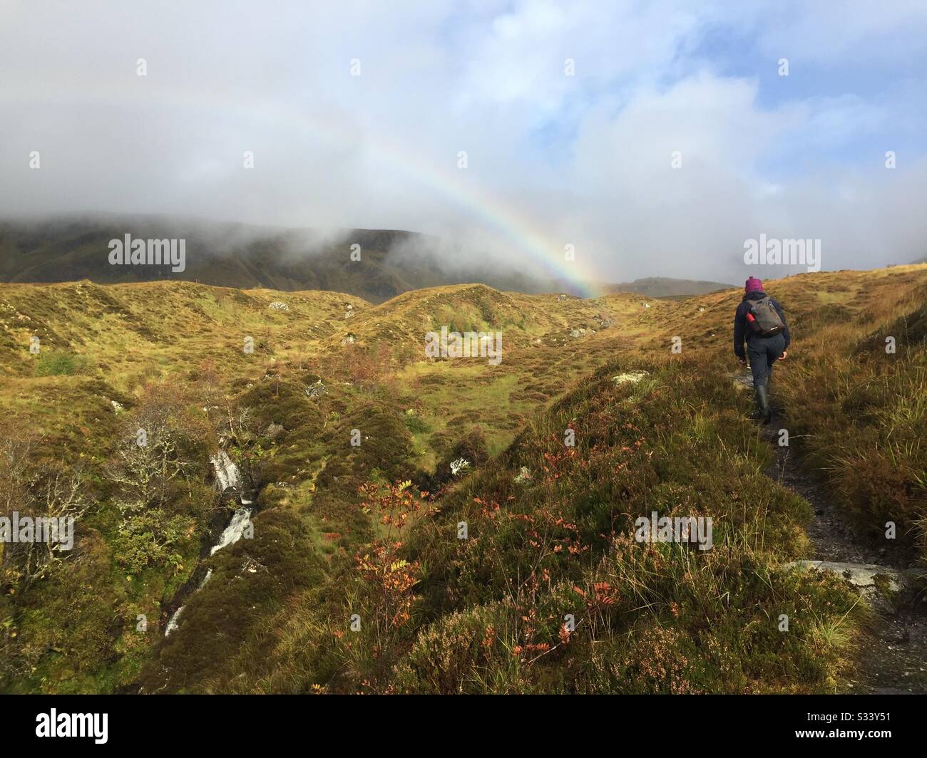 Hiking in Glen Affric, Scotland towards a rainbow in a hilly landscape Stock Photo