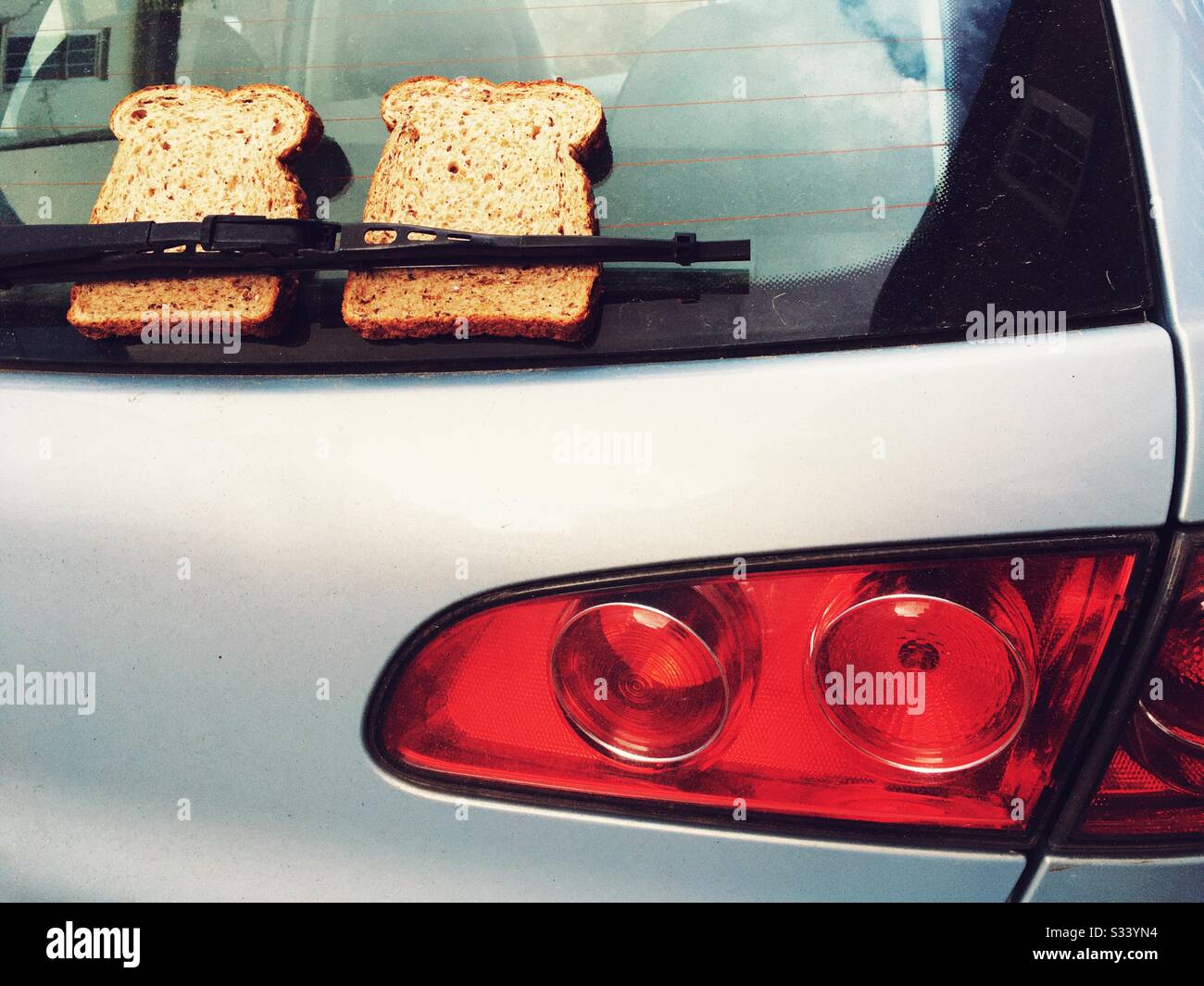 Brown sliced bread left under the rear window wiper blade of a Seat car. - Smartphone Captured Stock Image