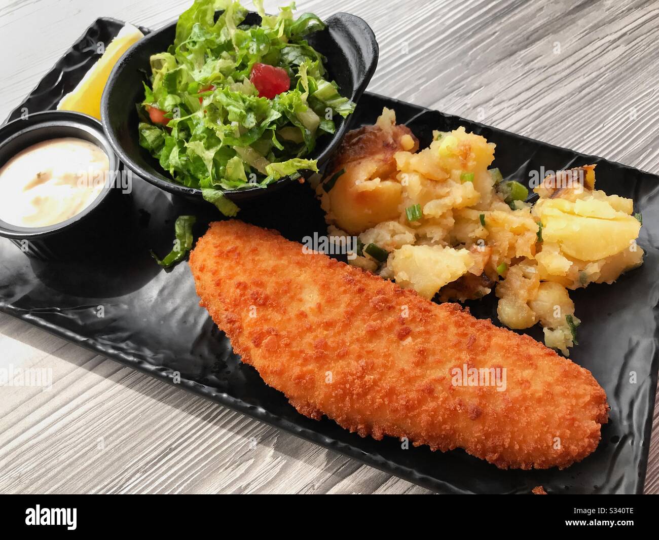 Breaded white fish with potatoes and fresh lettuce salad. - Smartphone Captured Stock Image