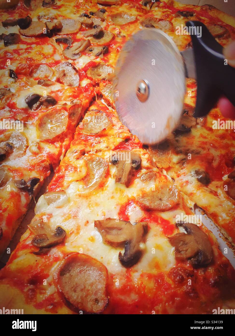Freshly baked pizza pie with sausage and mushroom toppings being sliced by a pizza cutting wheel Stock Photo