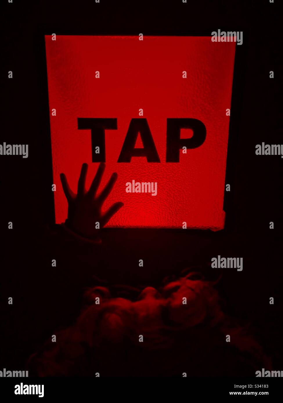 Red lit button with the word “Tap” and child’s hand silhouetted. - Smartphone Captured Stock Image