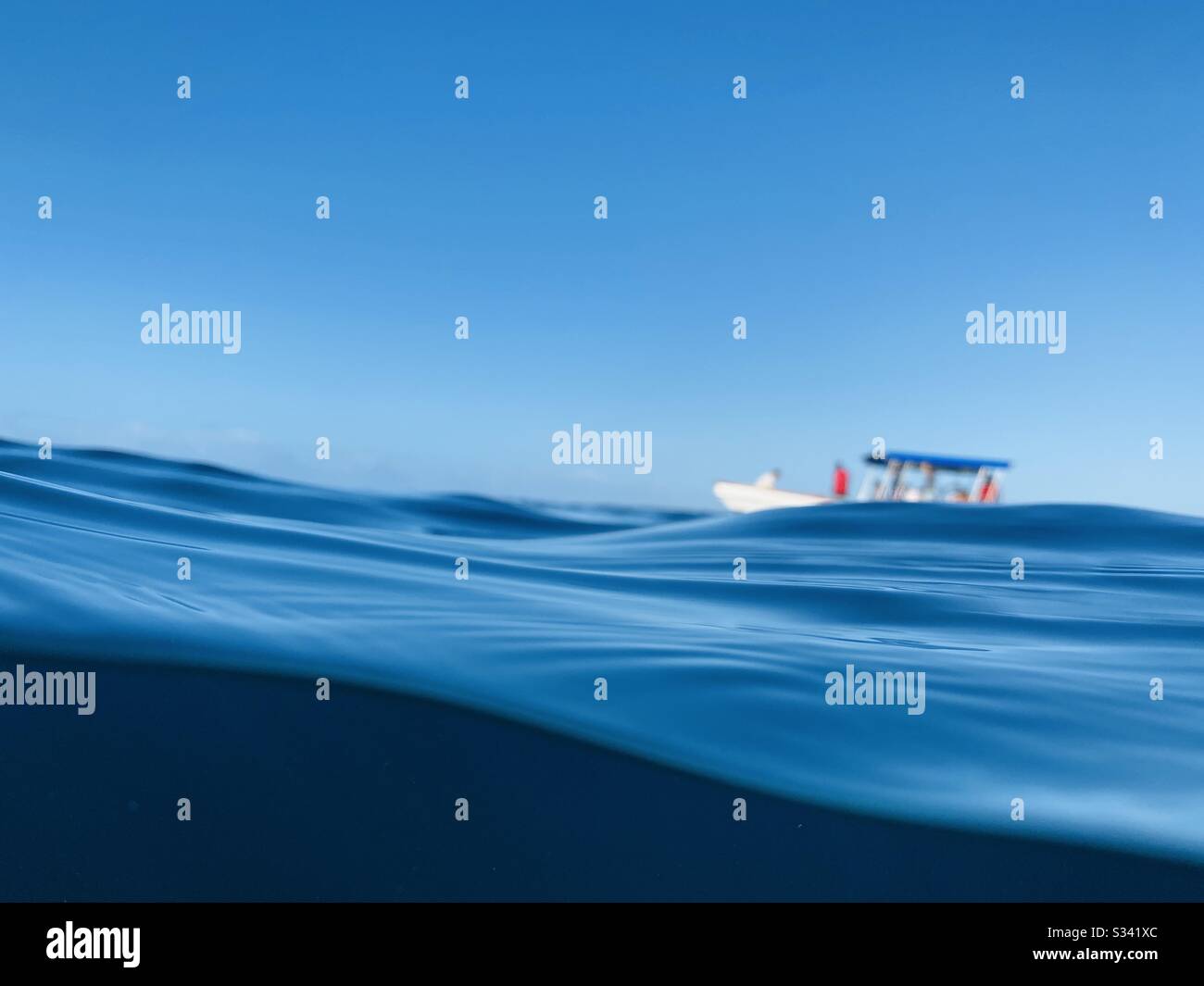 Overunder of a boat going out to the surf break. Cloudbreak, Fiji. - Smartphone Captured Stock Image