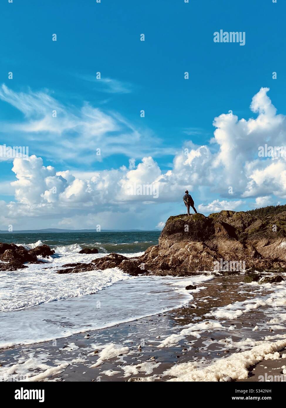 Man stands on rocky outcrop looking north to Juan de Fuca Strait, Whidbey Island, Washington State, USA - Smartphone Captured Stock Image