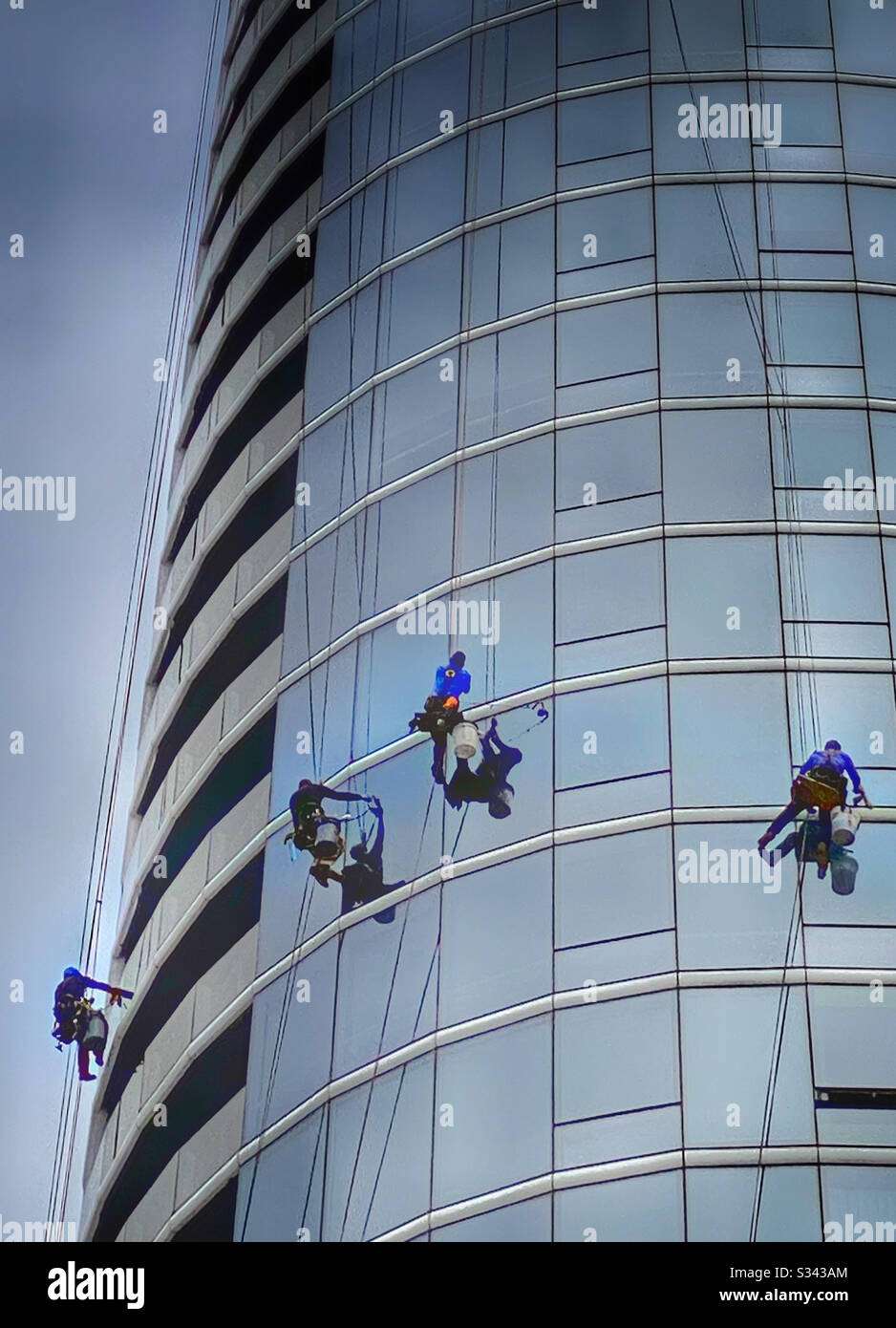 Window washers suspended on the facade of a steel and glass skyscraper - Smartphone Captured Stock Image