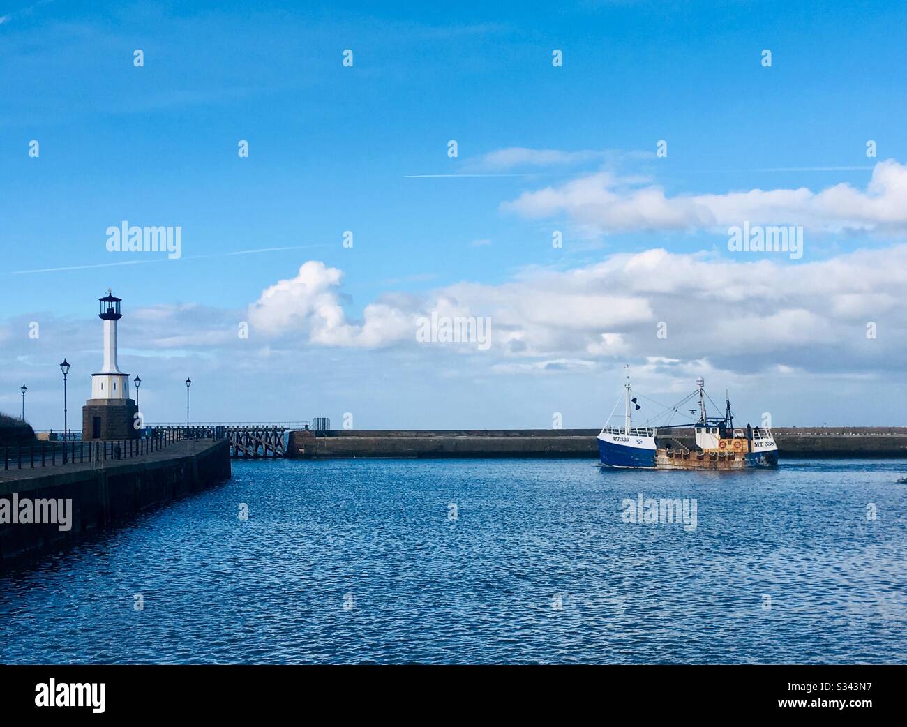 Fishing boat leaving the harbour passing the lighthouse at Maryport, Cumbria, England Stock Photo