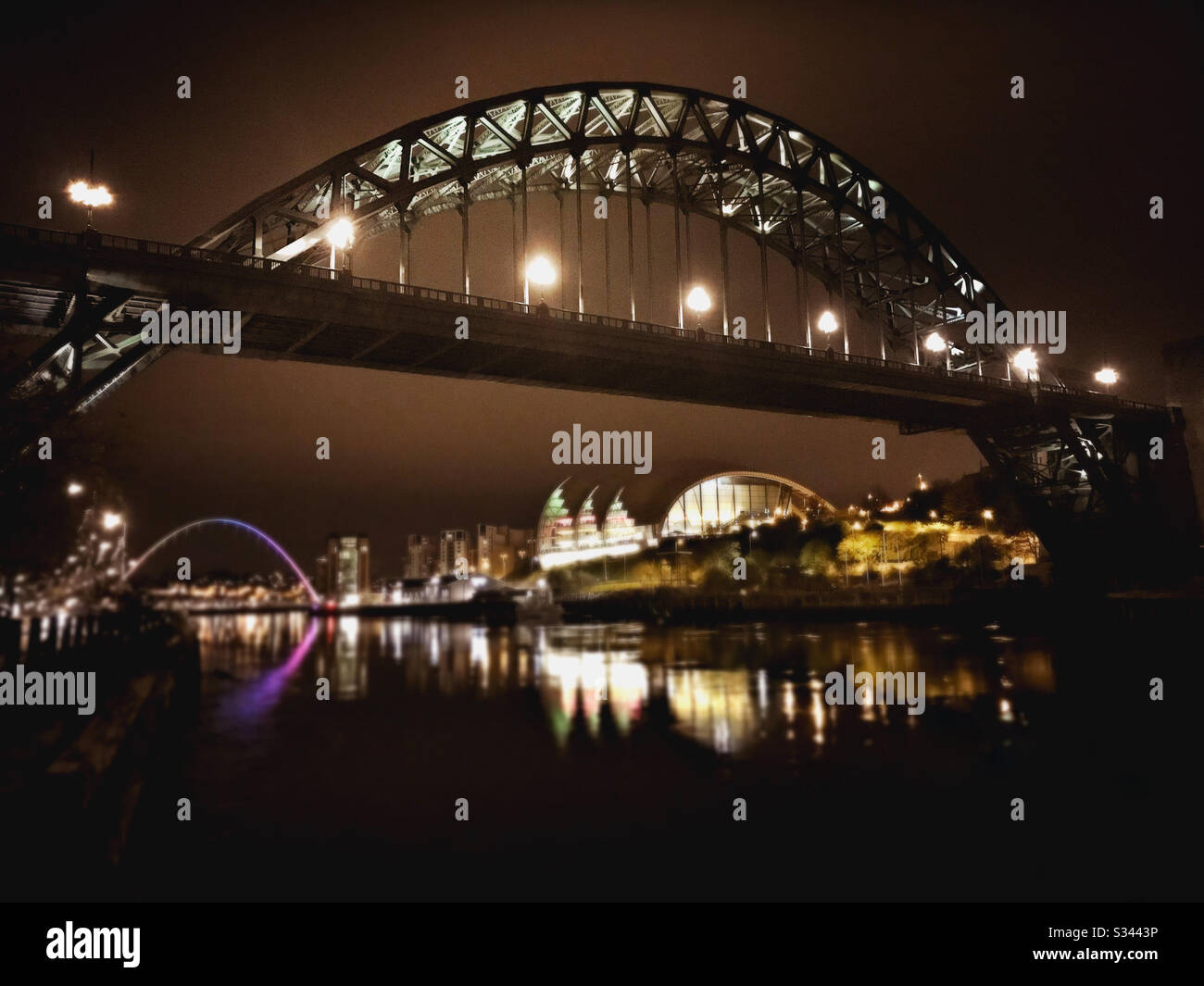 A night time view of the Tyne Bridge, Sage Gateshead and Millennium Bridge reflecting in the river Tyne in Newcastle upon Tyne, North East England - Smartphone Captured Stock Image