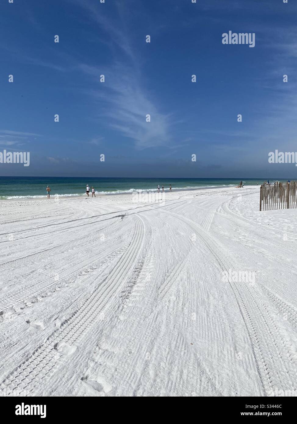People enjoying a walk on white sand beach along emerald water of the Gulf of Mexico - Smartphone Captured Stock Image