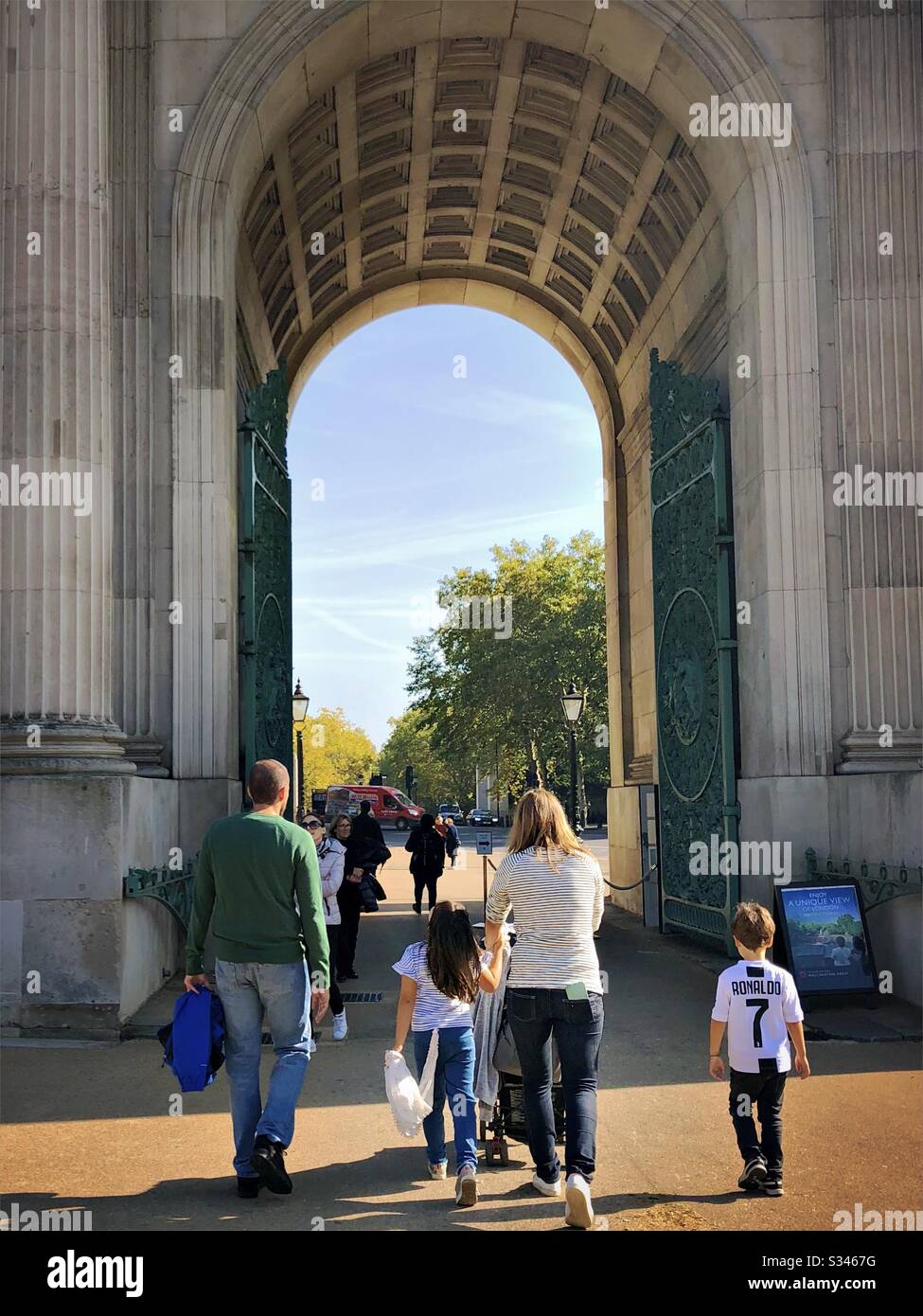 A young family are seen from behind, walking through gates of Wellington Arch, London. - Smartphone Captured Stock Image