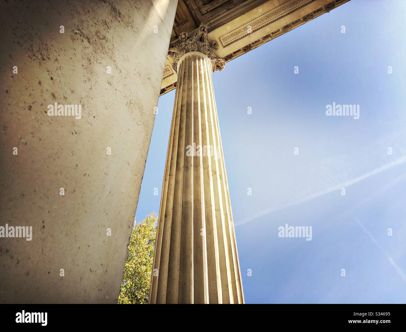 A low angle shot of a tall stone 19th century column against a blue sky. Architectural details of Wellington Arch, London - Smartphone Captured Stock Image