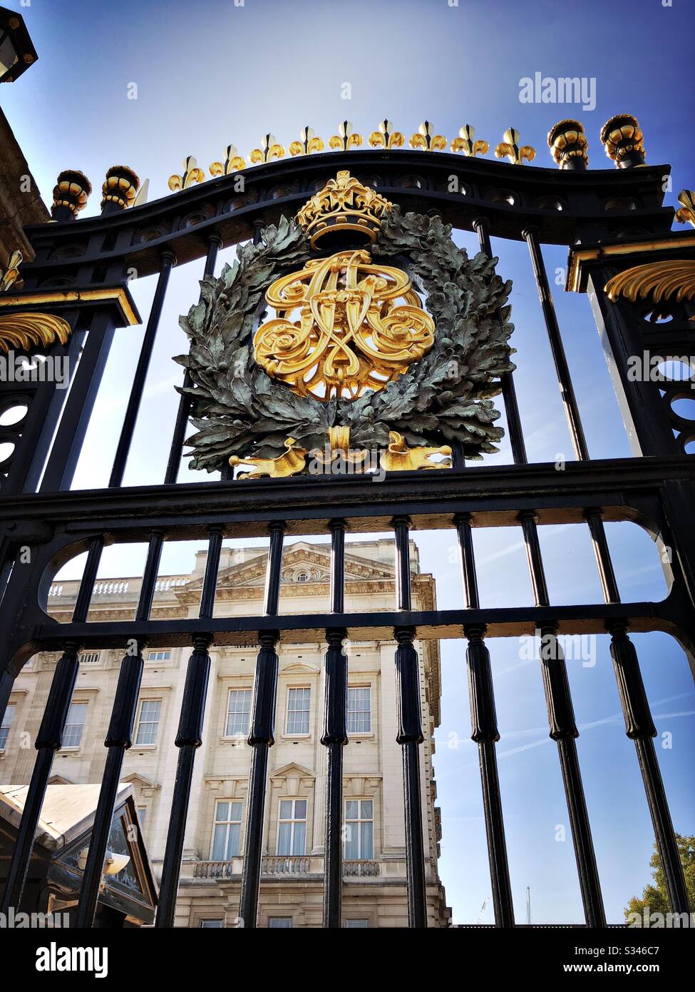 A close up and low angle shot of the black and gold metal railings with coat of arms at the gates to Buckingham Palace, London - Smartphone Captured Stock Image