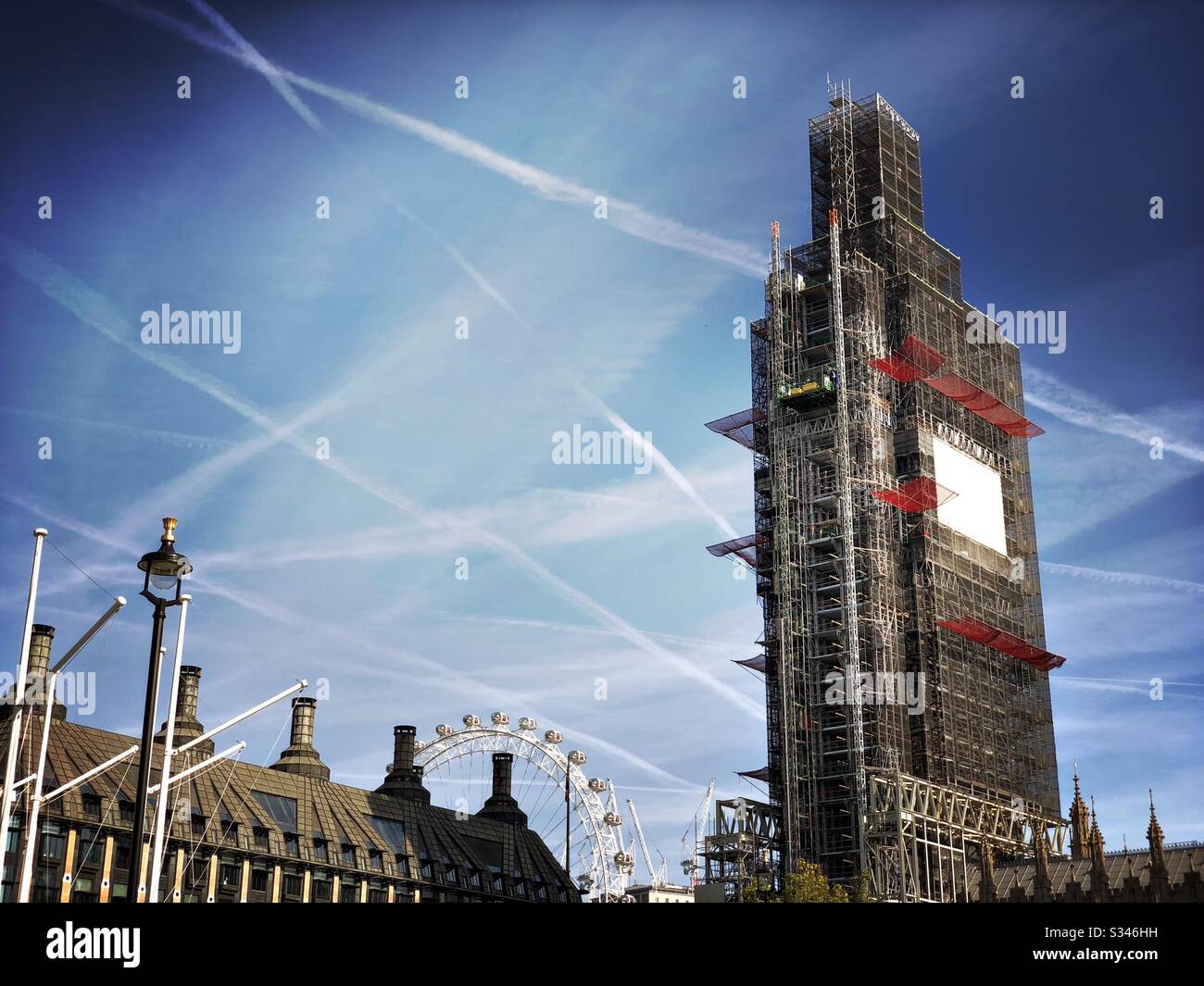 Many airplane contrails, vapid trails, are seen in a blue sky over scaffold covered Big Ben and the City of Westminster, London - Smartphone Captured Stock Image