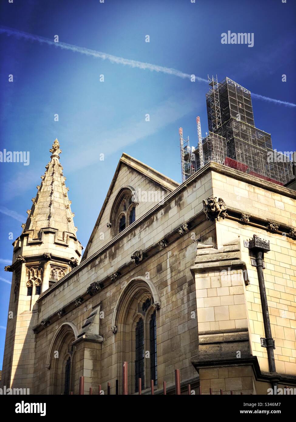 Architectural elements of the Palace of Westminster beneath a blue sky with plane contrails. Big Ben is seen in the background during renovation works at the Houses of Parliament, London - Smartphone Captured Stock Image