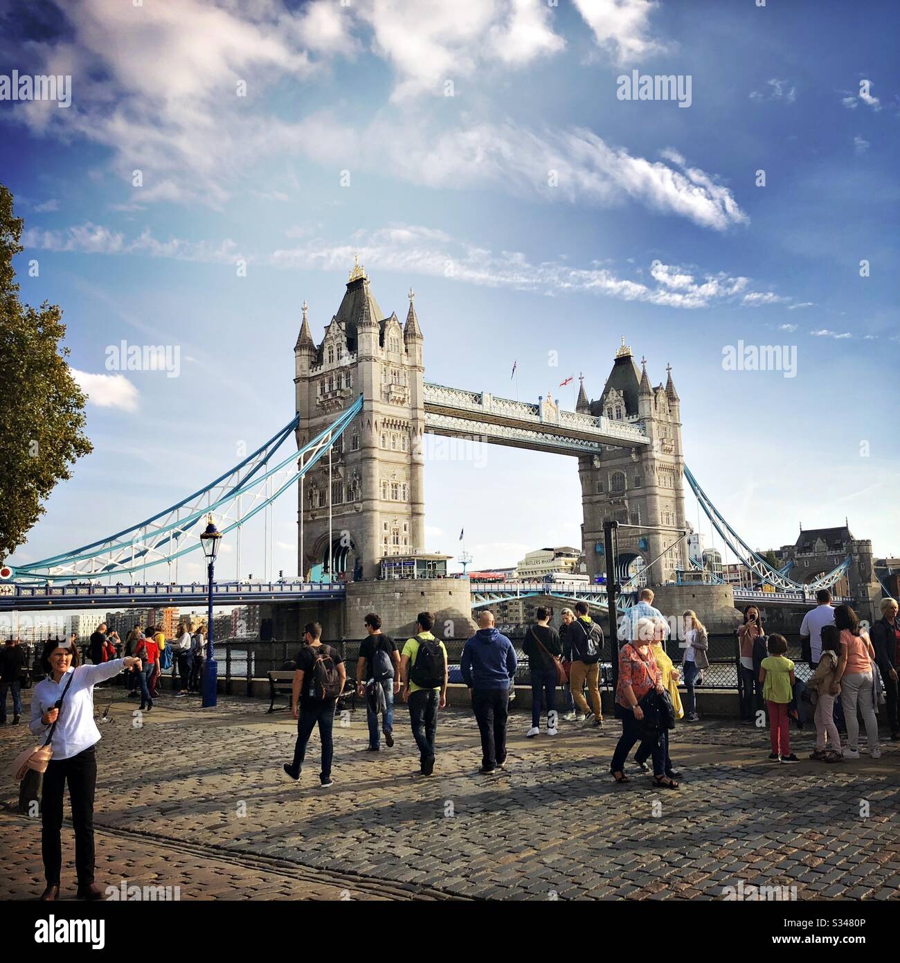 Tourists are seen by the River Thames and historic Tower Bridge, London - Smartphone Captured Stock Image