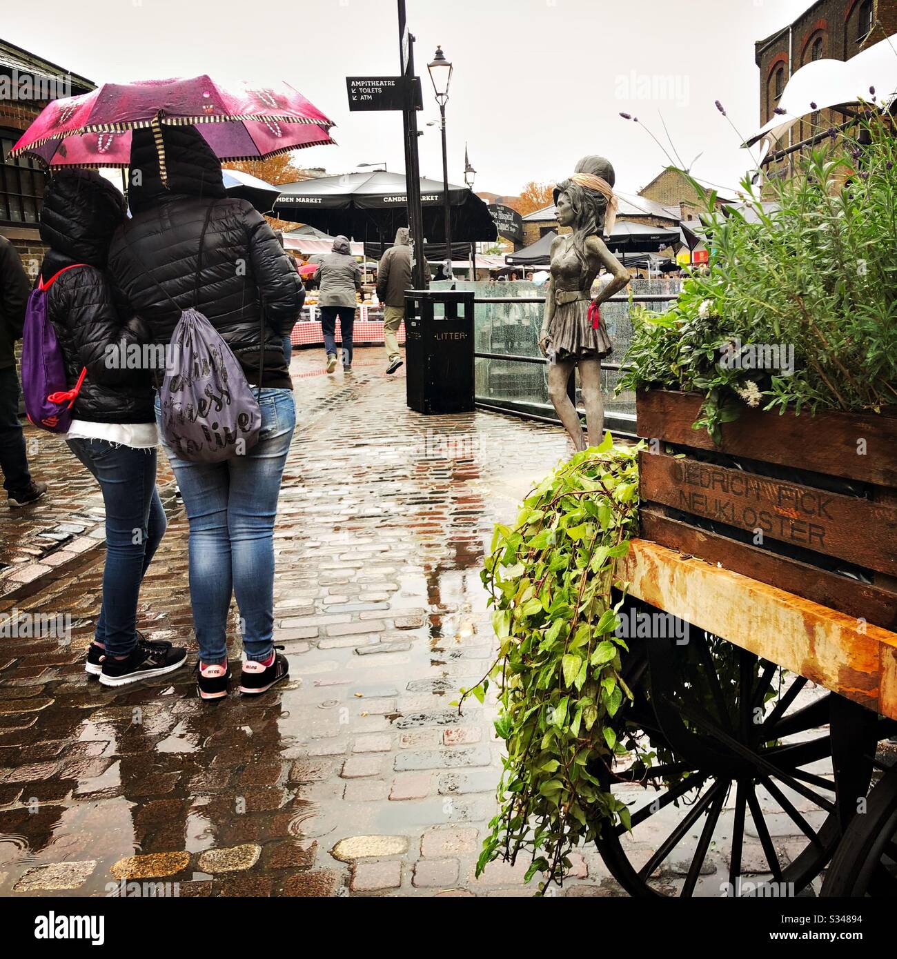 Tourists are seen taking photographs of the bronze statue of Amy Winehouse at Stables Market, Camden Town, London - Smartphone Captured Stock Image