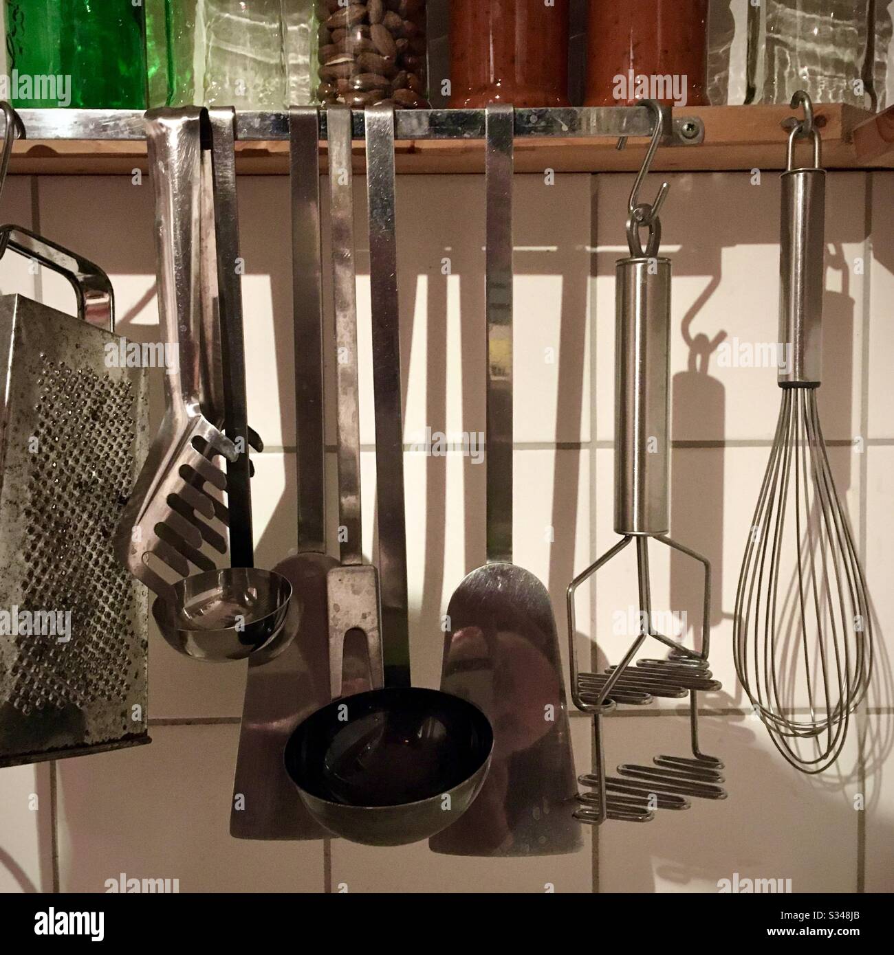 Kitchen utensils hang on a shelf with glass jars on it Stock Photo Alamy