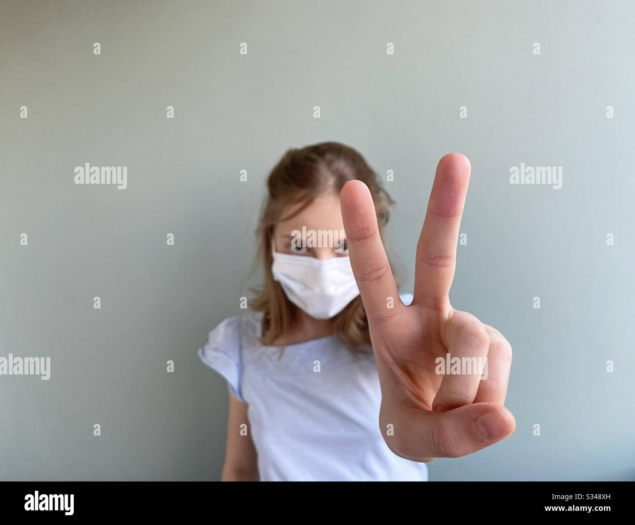 Victory sign shown by girl wearing surgical mask - Smartphone Captured Stock Image