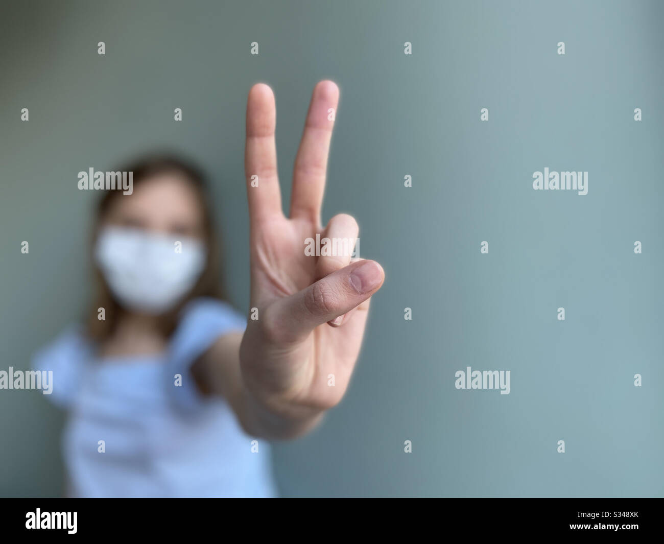Victory sign shown by girl wearing surgical mask - Smartphone Captured Stock Image