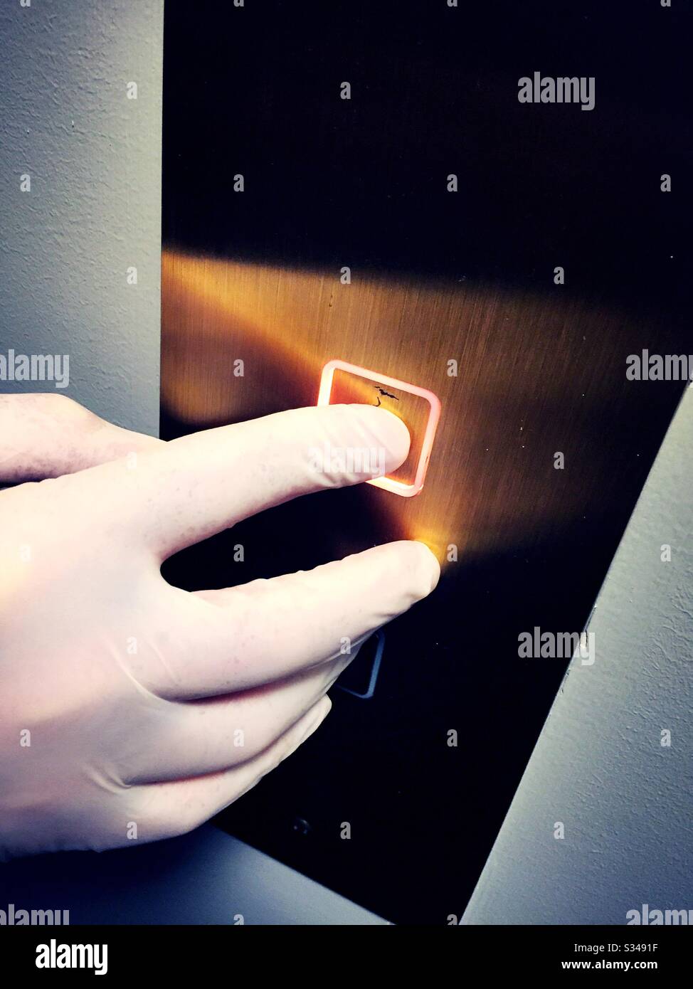 Health precaution practiced by a man wearing a plastic glove to prevent spread of COVID-19 virus in pushing an elevator button, NYC, USA - Smartphone Captured Stock Image