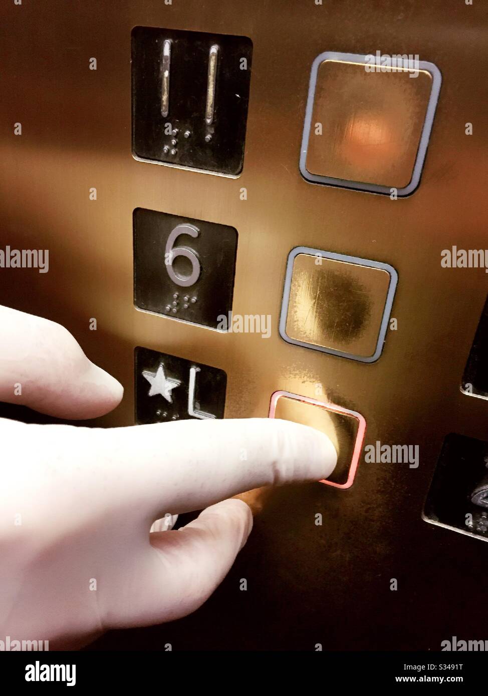 Coronavirus prevention being practiced by a man wearing a latex glove pushing an elevator button to prevent the spread of the virus germs, USA - Smartphone Captured Stock Image