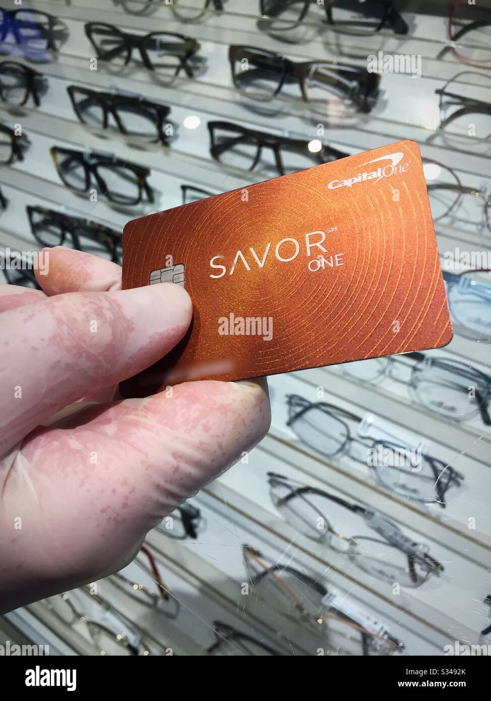 Gloved hand holding credit card when paying for eyeglasses during the coronavirus pandemic in order to prevent the spread of the virus, USA - Smartphone Captured Stock Image