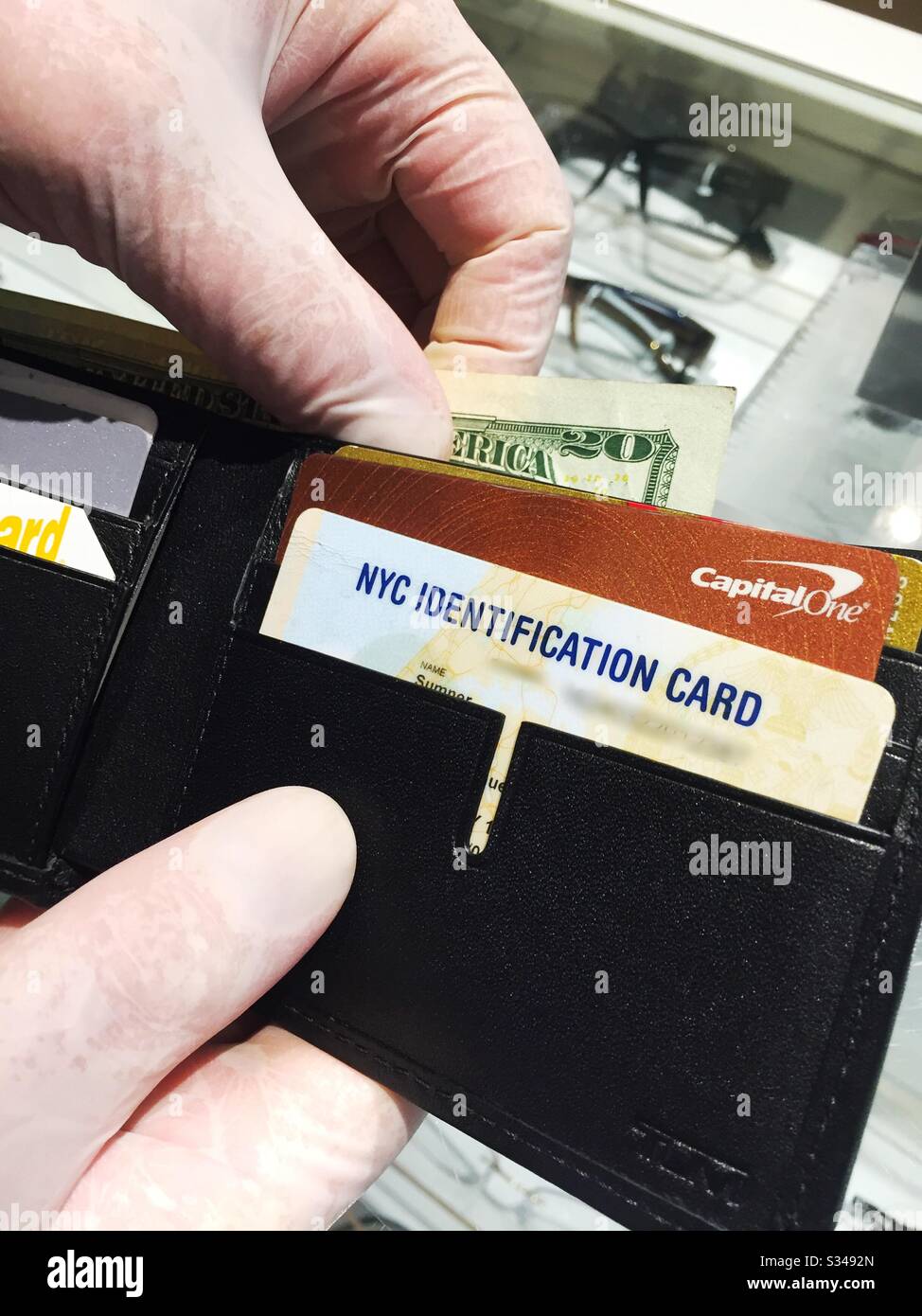 A man wearing latex glove to prevent spread of the coronavirus opens his wallet when buying eyeglasses at a store in New York City, USA - Smartphone Captured Stock Image