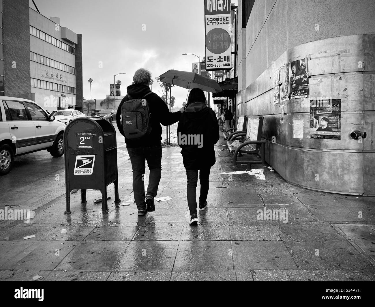 LOS ANGELES, CA, MAR 2020: young couple with man carrying umbrella over his girlfriend as they walk through wet streets in Korea Town Stock Photo