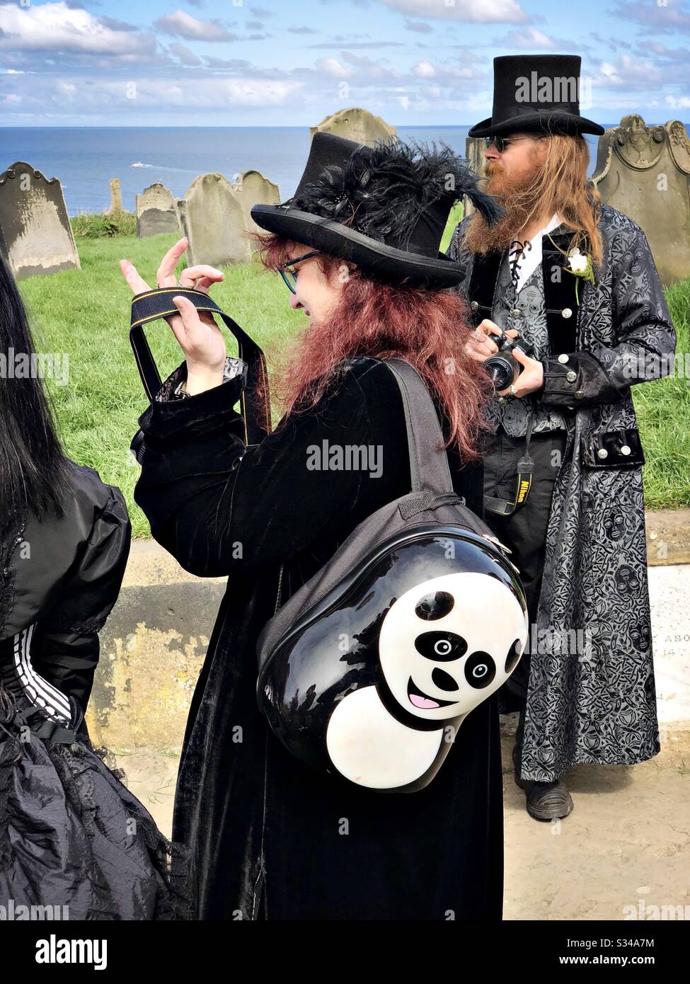 A girl is seen dressed in a goth costume wearing a panda backpack during the Whitby Goth Weekend cosplay event - Smartphone Captured Stock Image