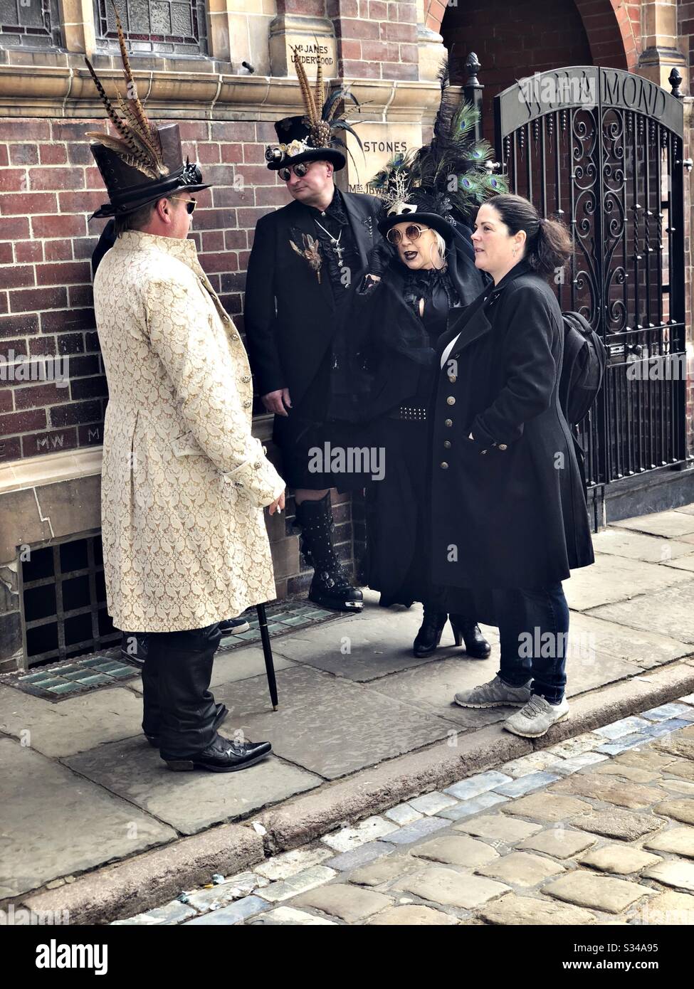 People in creative costumes during a cosplay event. Whitby Goth Weekend. Group of steampunks chat in street - Smartphone Captured Stock Image