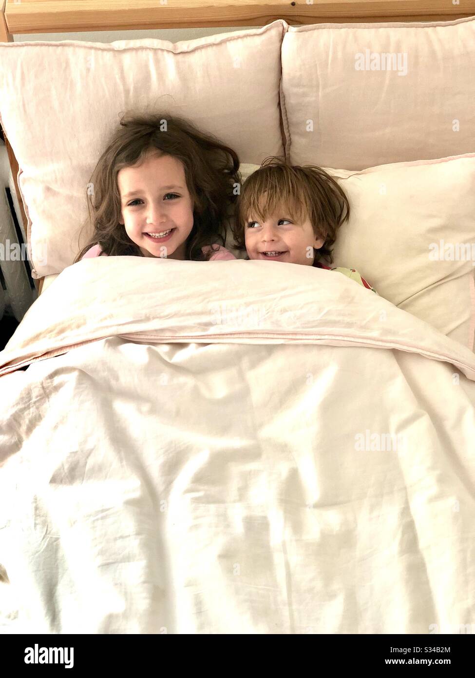 Six year old sister cuddling with her two-year-old baby brother under the covers and giggling. - Smartphone Captured Stock Image