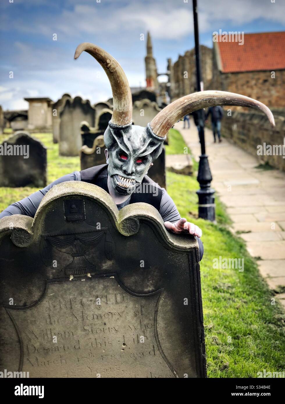 Person in a creative costume during a cosplay event. Whitby Goth Weekend. Man in monster mask and horns, demon at graveyard - Smartphone Captured Stock Image