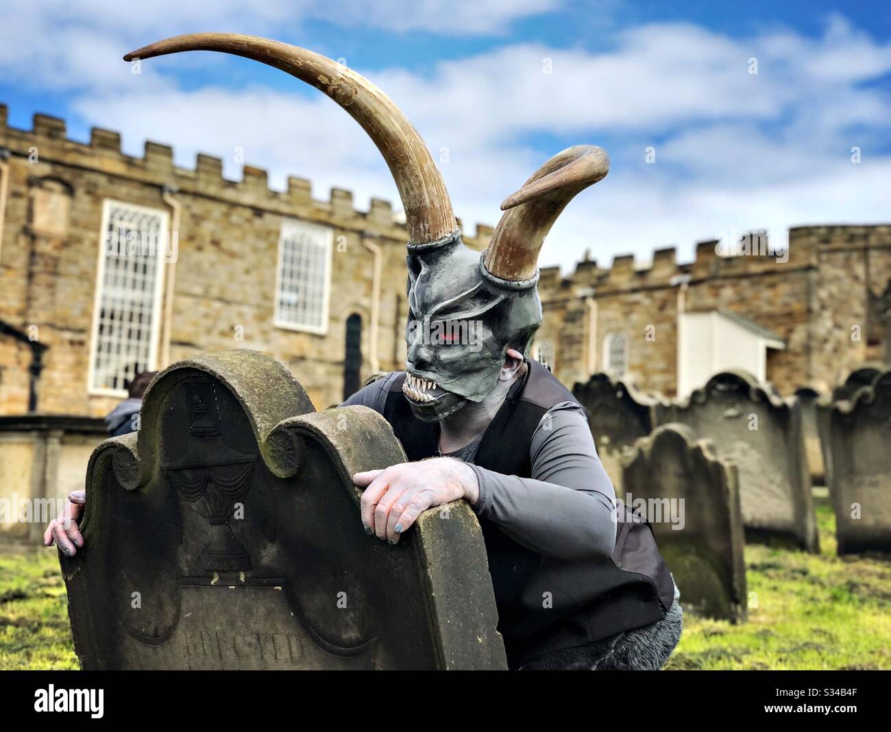 Person in a creative costume during a cosplay event. Whitby Goth Weekend. Man in monster mask and horns, demon at graveyard - Smartphone Captured Stock Image