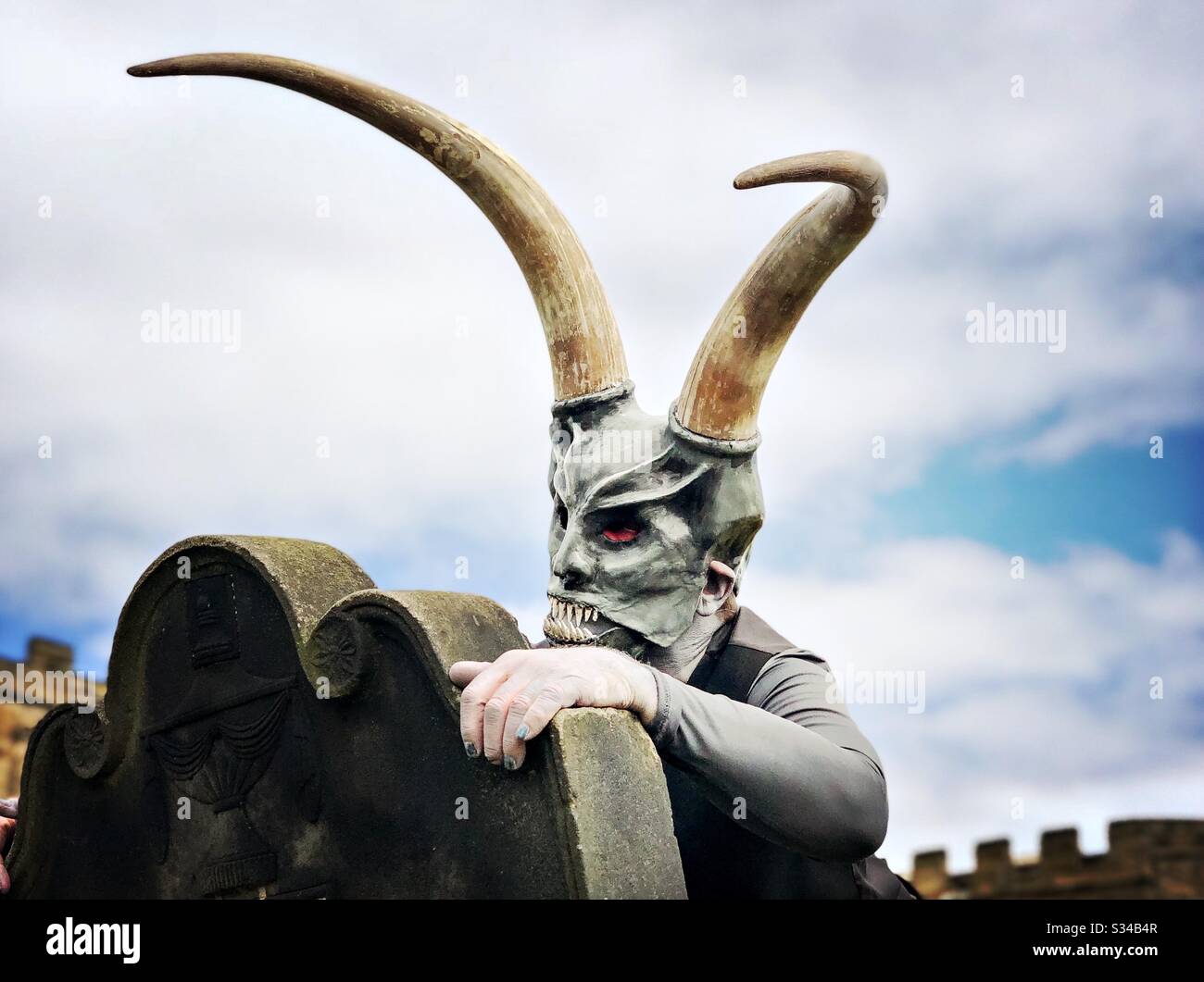 Person in a creative costume during a cosplay event. Whitby Goth Weekend. Man in monster mask and horns, demon at graveyard - Smartphone Captured Stock Image