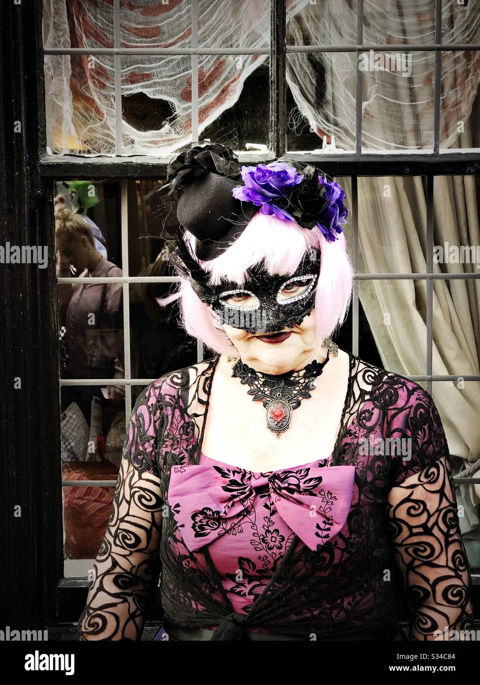 Person in a creative costume during a cosplay event. Whitby Goth Weekend. Woman in vintage gothic outfit against weathered window - Smartphone Captured Stock Image