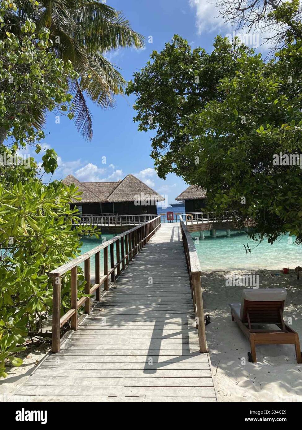 Tropical beach view of wooden bridge leading to bungalows in shallow water in the Maldives - Smartphone Captured Stock Image