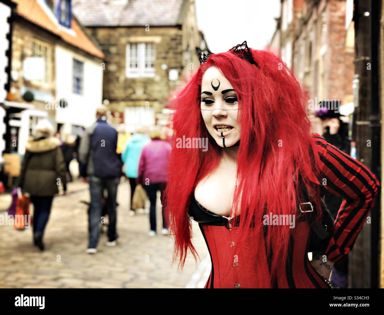 Person in a creative costume during a cosplay event. Whitby Goth Weekend. Gothic girl in red and black leather adjusts costume - Smartphone Captured Stock Image