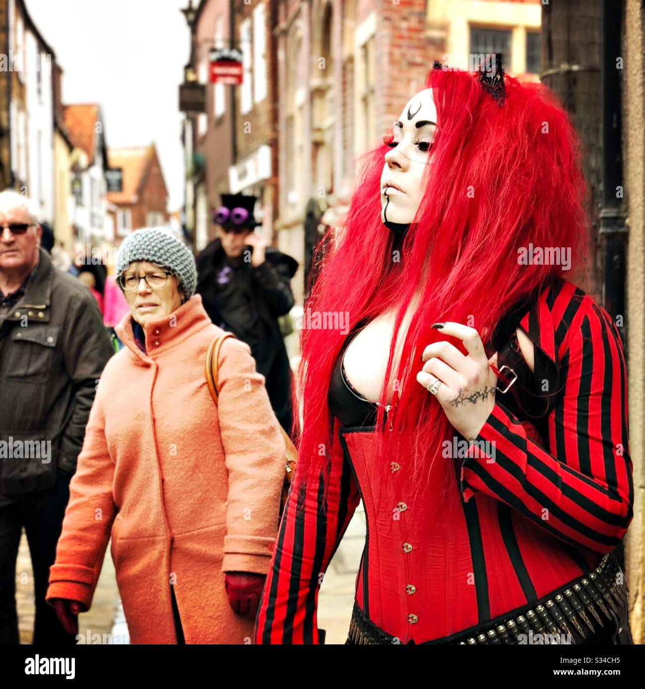 Person in a creative costume during a cosplay event. Whitby Goth Weekend. Confident girl in red and black leather catsuit - Smartphone Captured Stock Image
