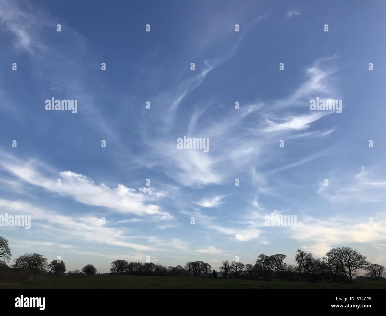 Swirling clouds in a blue sky above fields and trees - Smartphone Captured Stock Image