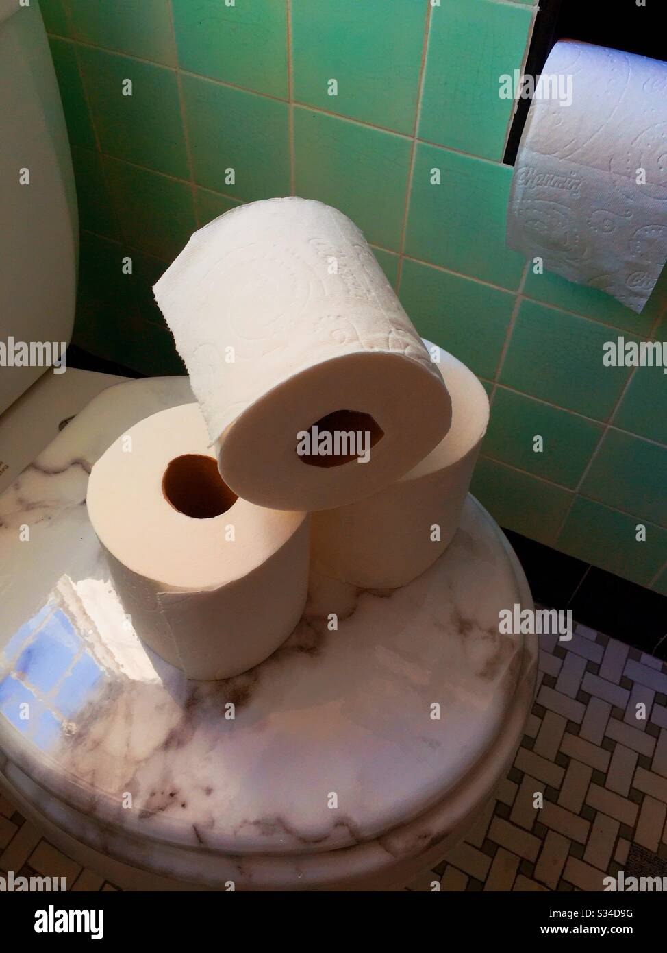 Toilet paper Rolls stacked on a toilet seat lid in a green tiled residential bathroom, USA Stock Photo