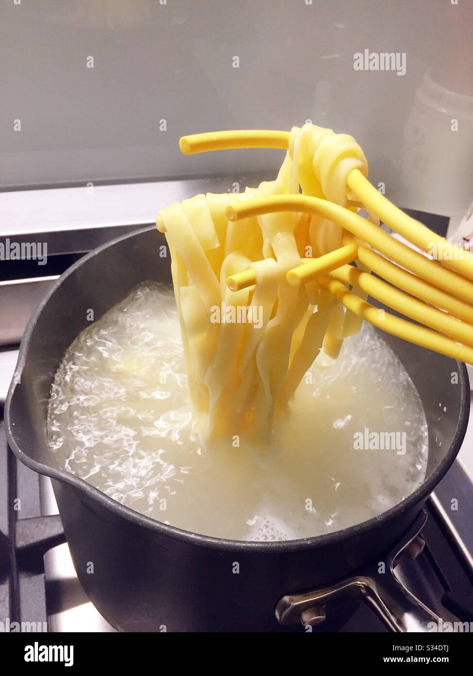 Wooden pasta fork holding freshly prepared spaghetti noodles on a residential kitchen stove, USA - Smartphone Captured Stock Image