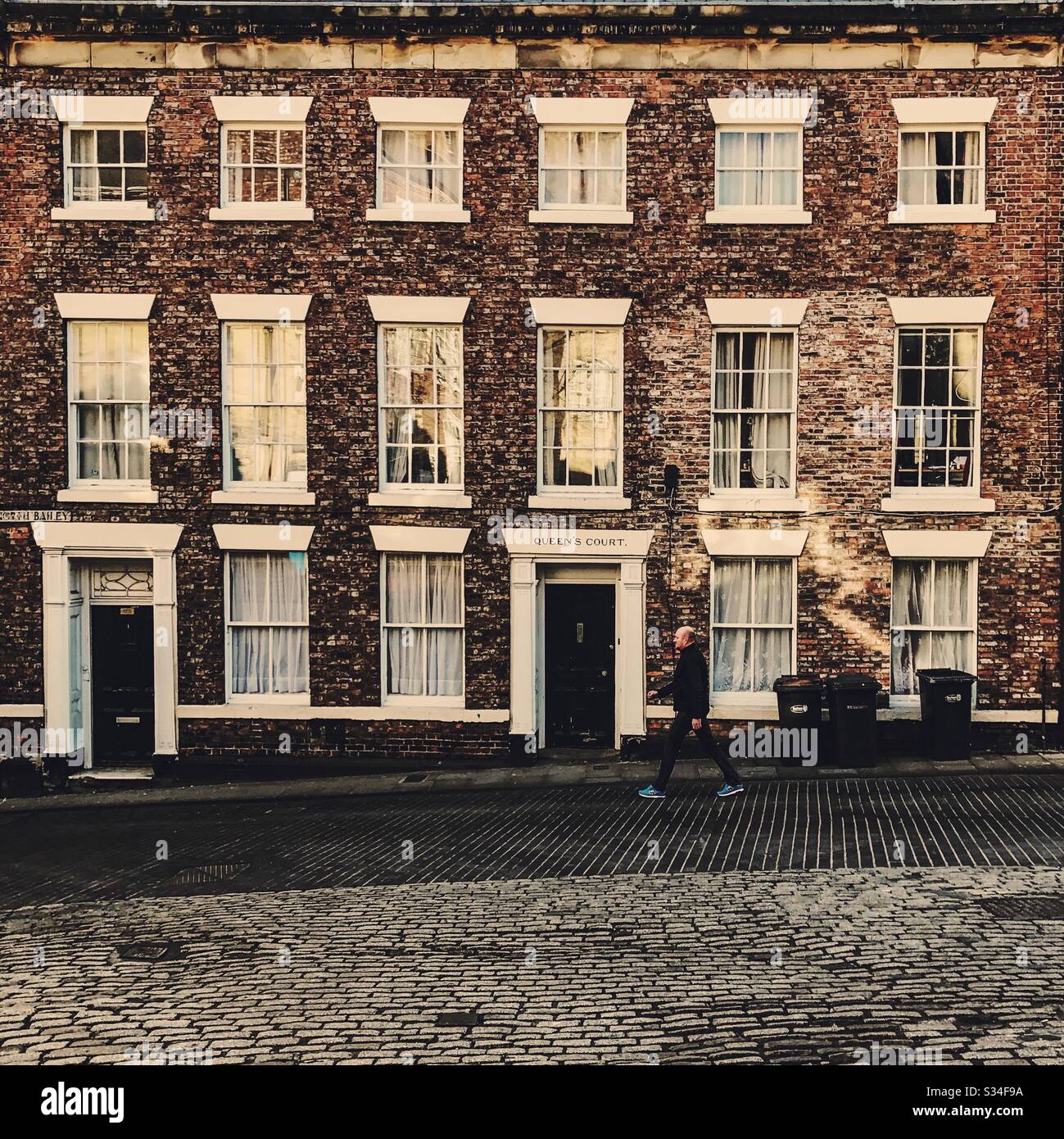 Architecture of Durham City, North East England. Man walks by old brick building. Queen’s Court, Saddler Street. - Smartphone Captured Stock Image