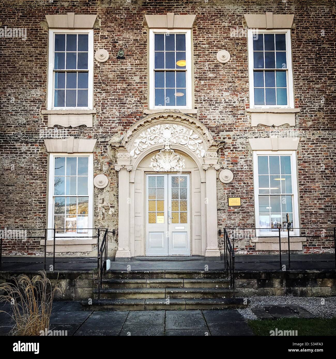 Architecture of Durham City, North East England. Intricate stone door surround painted cream and white with Georgian sash windows and rustic brickwork - Smartphone Captured Stock Image